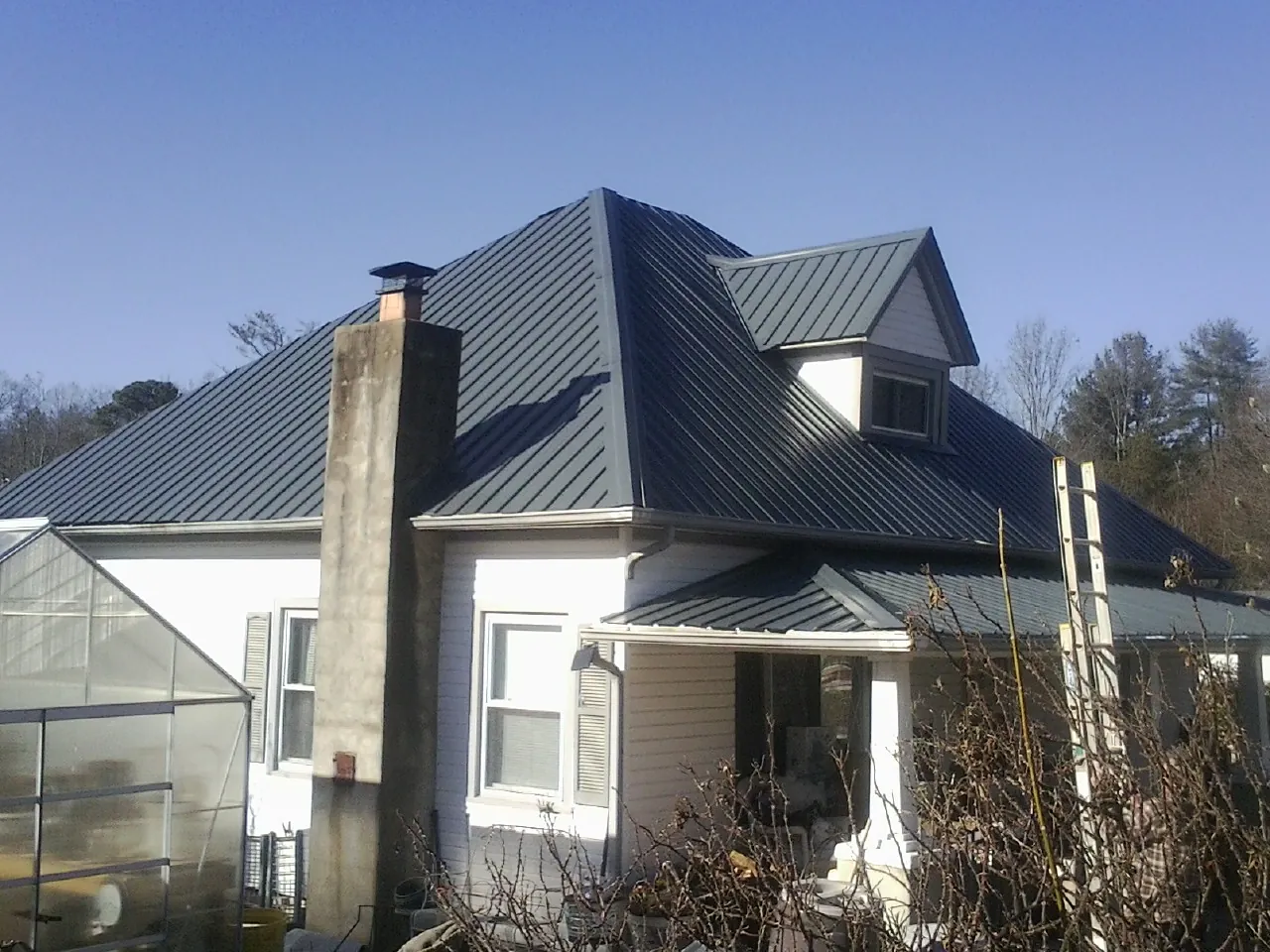 Dark blue standing seam metal roof on a white farmhouse with dormer — Slate & Tile Roof Repair by Roofing Brothers in Poultney