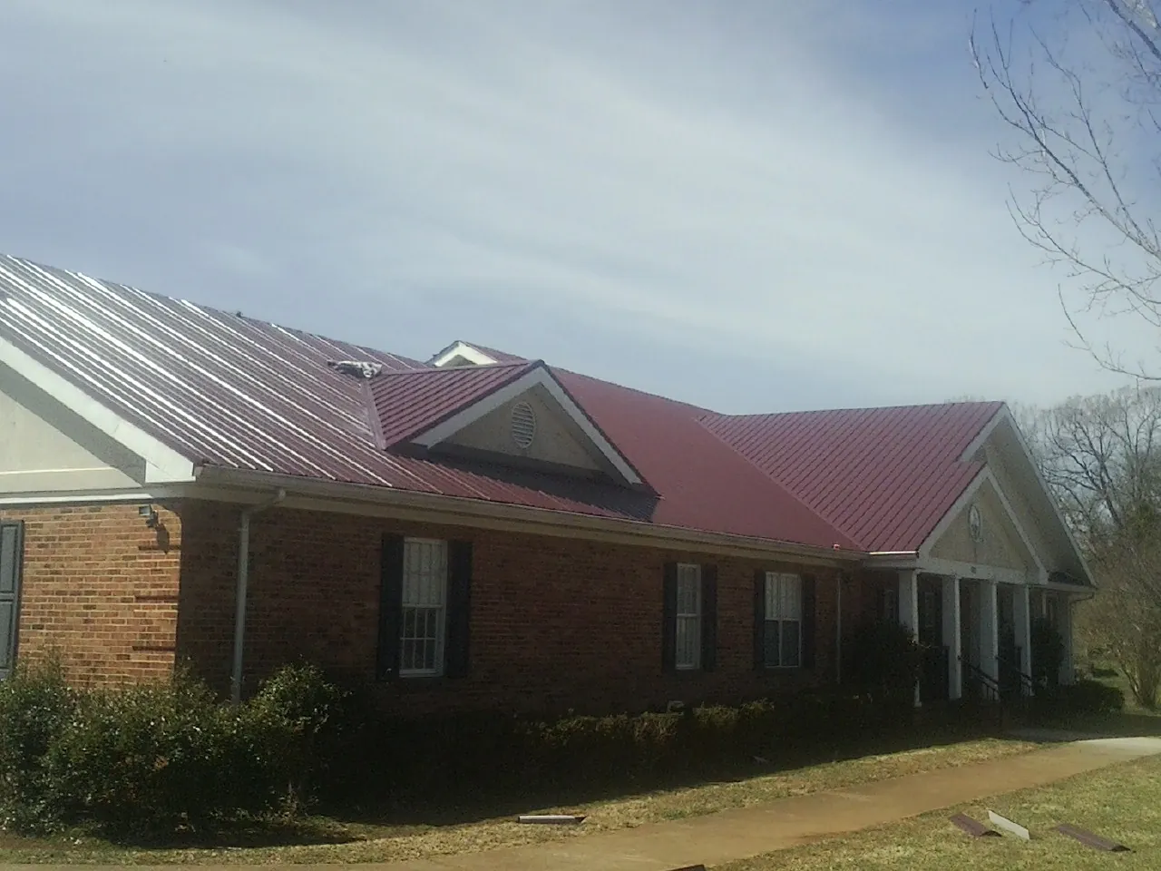 Red metal roof with gabled entries on a long brick building, from a Hail Damage Roof Repair job in Poultney