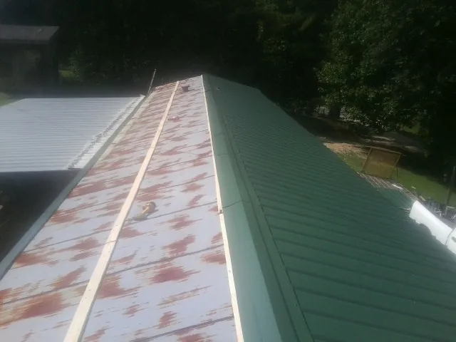 Old rusted panels beside newly installed green metal roofing — Wind Damage Roof Repair by Roofing Brothers in Poultney