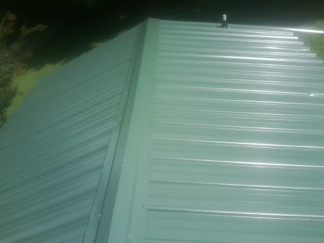 New green metal panels meeting at the ridge of a roof — Flat Roof Repair work by our crew in Poultney