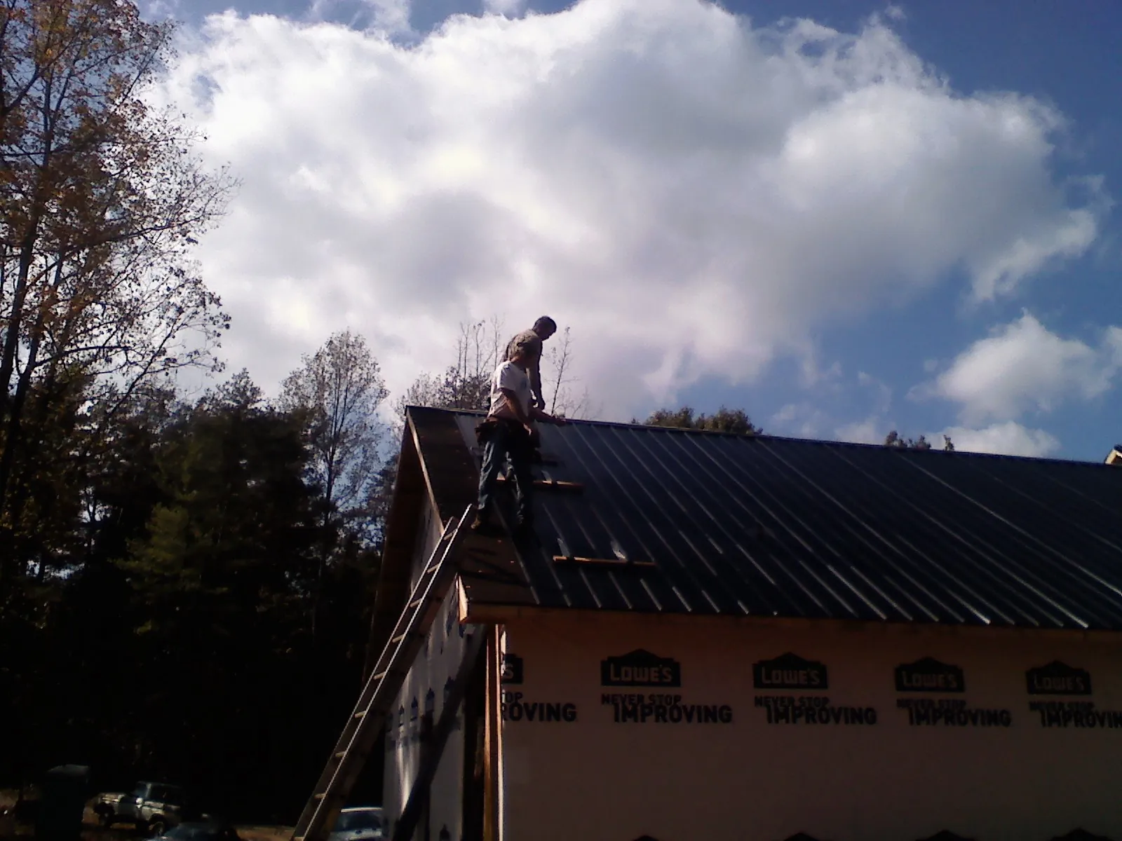 Roofer fastening dark metal panels high against a cloudy sky, from a Roof Inspection job in Poultney
