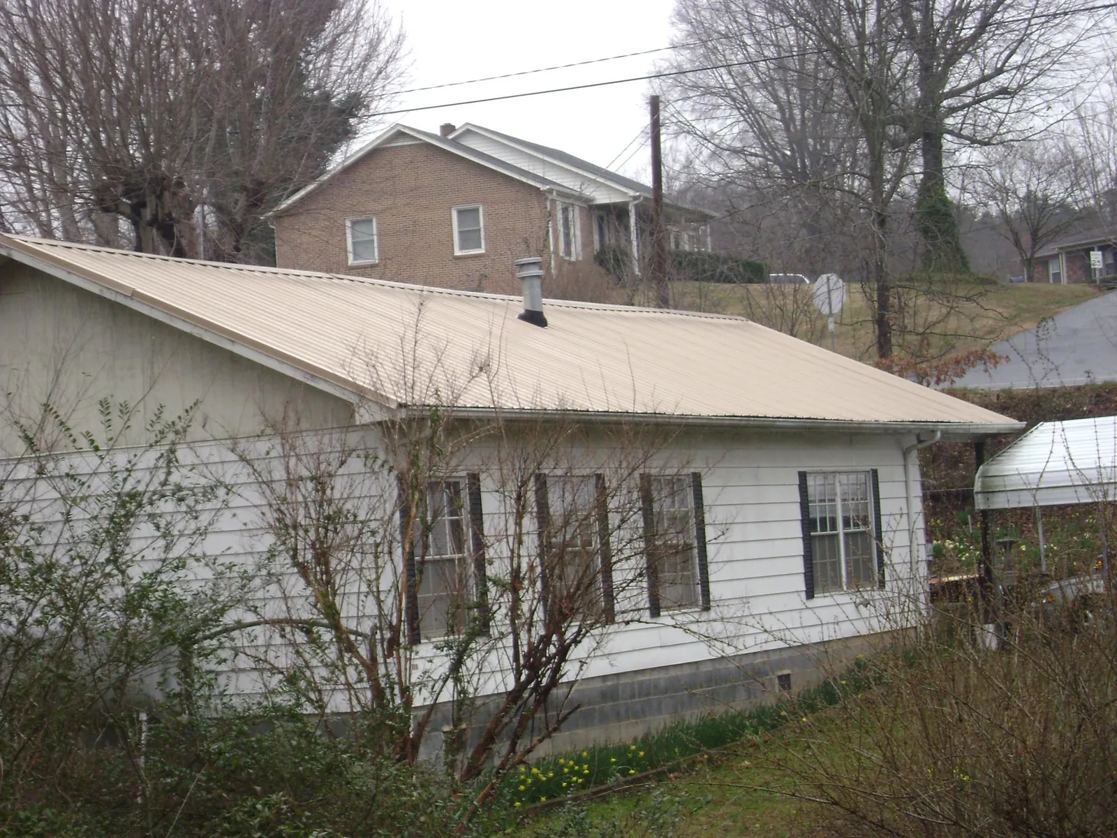 Tan metal roof on a white sided house set into a hillside — Commercial Roofing by Roofing Brothers in Poultney